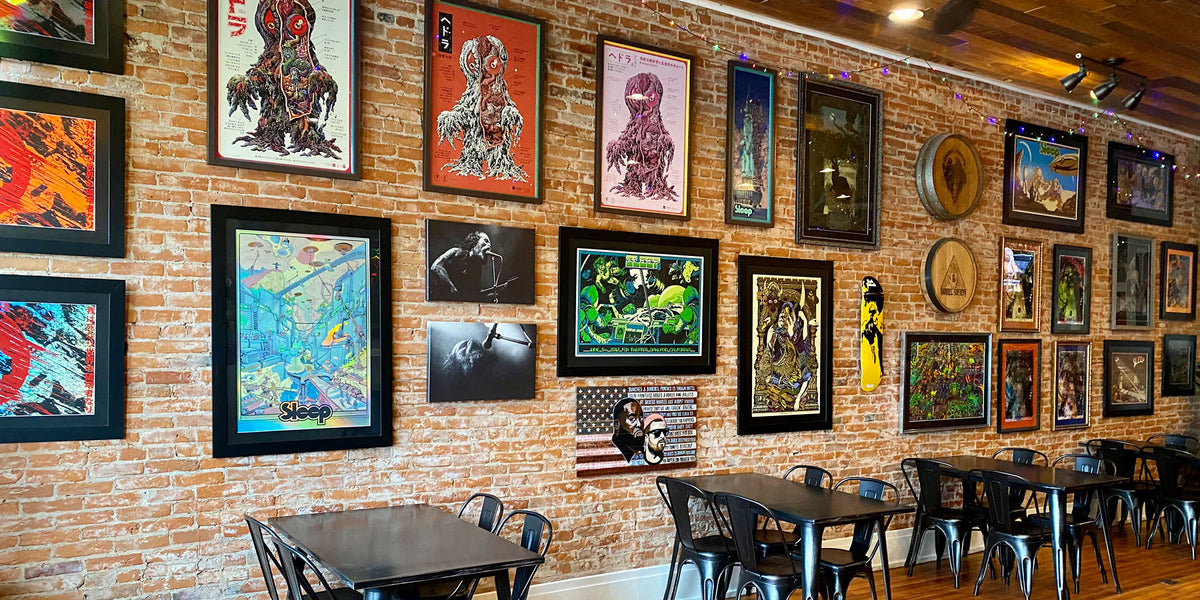 Custom gallery wall at Barrel Society in Princeton, Illinois, featuring an eclectic collection of framed artwork, concert posters and photography displayed on an exposed brick wall.