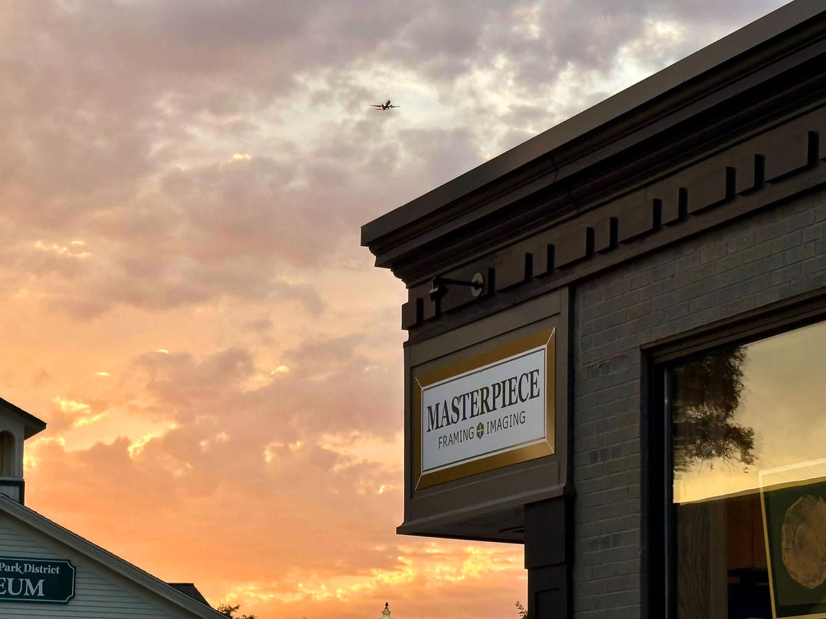 Masterpiece Framing + Imaging storefront in Bloomingdale, Illinois, with its gold-framed sign against a vibrant sunset sky.