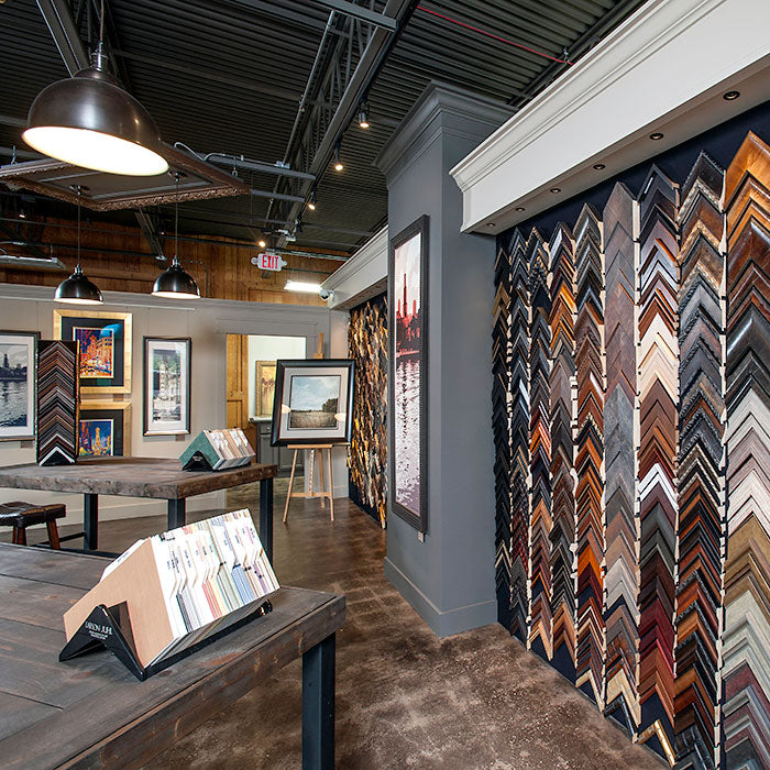 Interior of Masterpiece Framing & Imaging's showroom featuring an extensive wall of custom picture frame moulding samples, framed artwork and design tables.