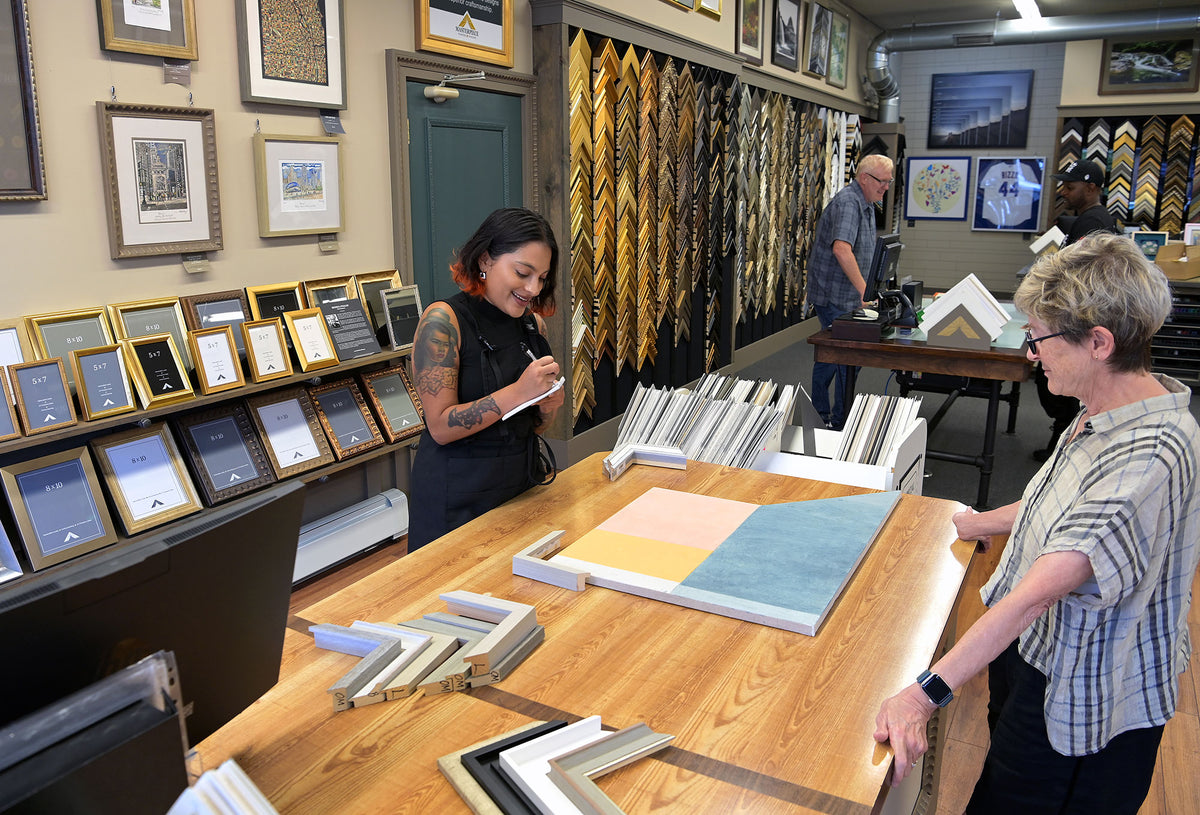 Custom framing consultation at Masterpiece Framing & Imaging in Evanston, Illinois, with a designer reviewing frame samples and mat colors with a customer.