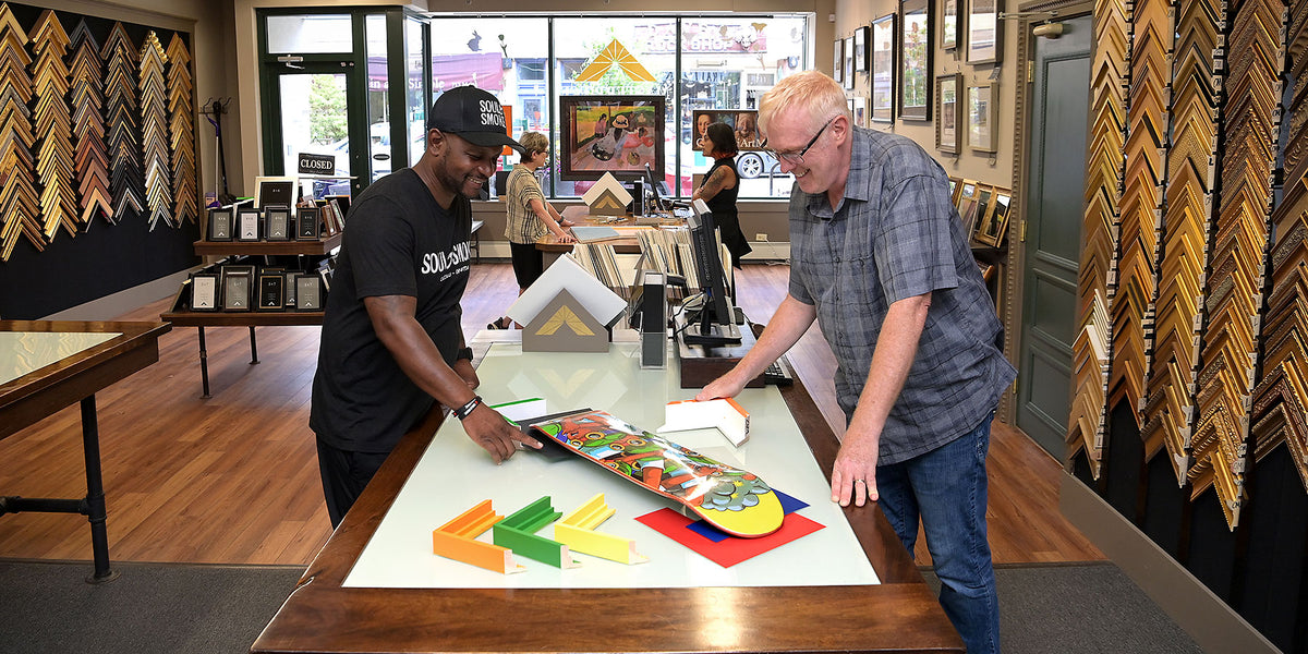 Customer and framing designer review colorful frame samples and matting options for a custom-framed skateboard at Masterpiece Framing & Imaging in Evanston.