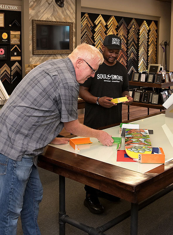 A framing designer and customer compare colorful frame moulding samples for a skateboard display at Masterpiece Framing & Imaging in Evanston.