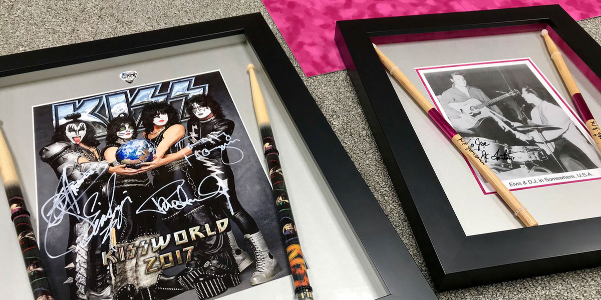 Custom black shadowbox frames displaying autographed KISS band photographs, drumsticks and a guitar pick alongside framed music memorabilia.
