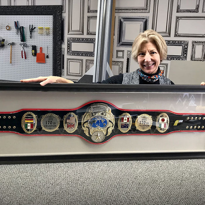 Masterpiece Framing team member in workshop holding custom framed championship belt display.
