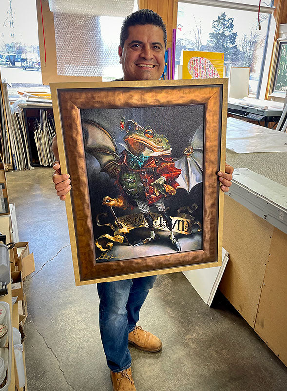 Masterpiece Framing team member holding a custom framed artwork inside the workshop.